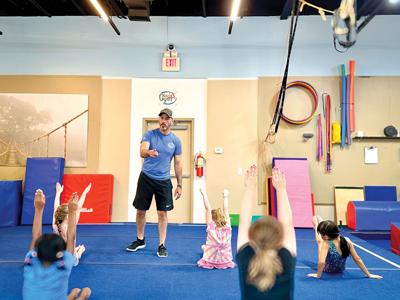 A gymnastics coach points into the crowd of young students raising their hands