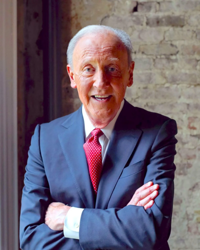 Frank Bumstead wearing a blue suit and red tie looking into camera