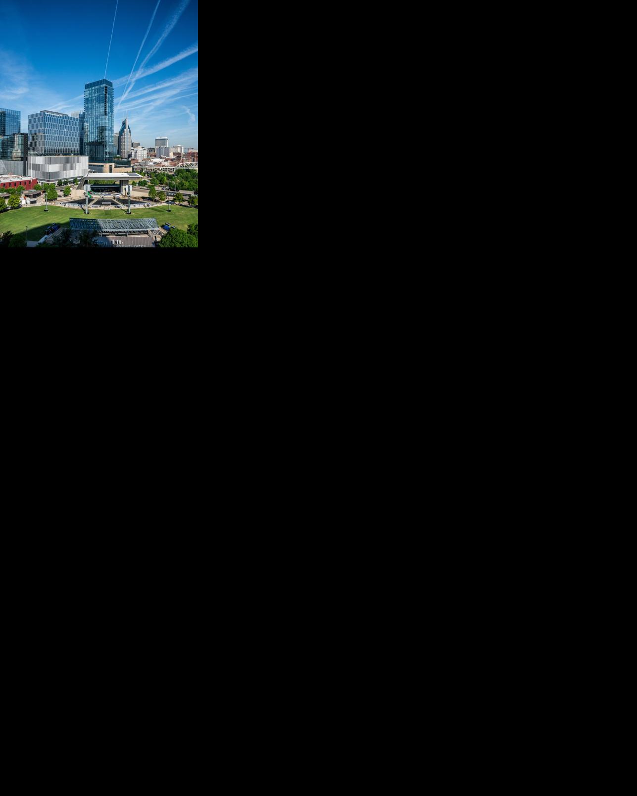A view of downtown Nashville on a sunny day, with several office buildings, the roof over the stage at Ascend Amphitheater and the John Seigenthaler Pedestrian Bridge all visible