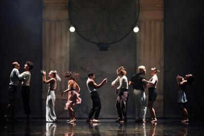 A row of dancing couples on stage in front of two columns and a wall covered in graffiti
