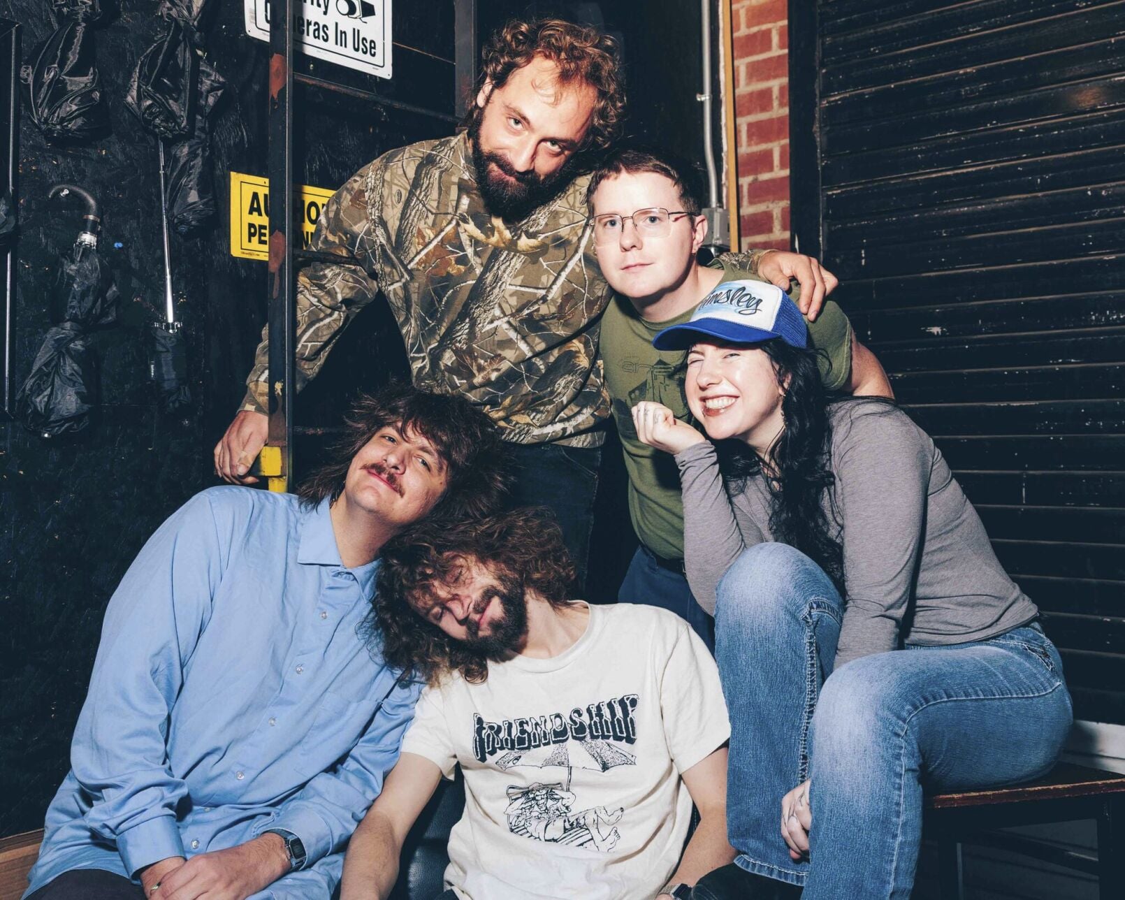 2026 color press photograph of the band Wednesday, posing near a fire escape ladder and a display of folded black umbrellas hanging on a wall