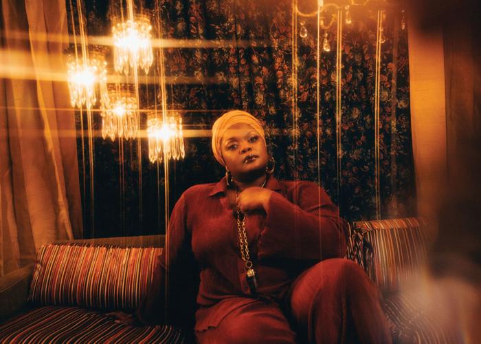 Kyshona press photo artist sits on a couch beneath twinkling lights