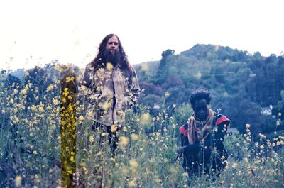 Musician Carlos Niño and poet Saul Williams stand in a field of yellow wildflowers