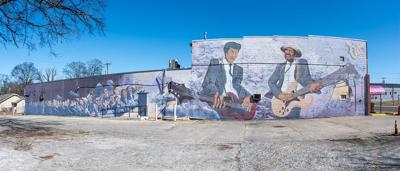 A mural on the side of a building showing fans in the stands on the left of the mural and and two guitarists on the right, playing their instruments facing each other.