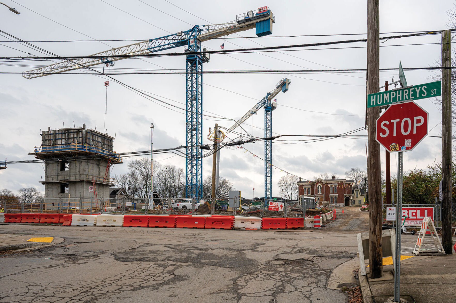 A pair of cranes loom over an unfinished building behind orange barricades.