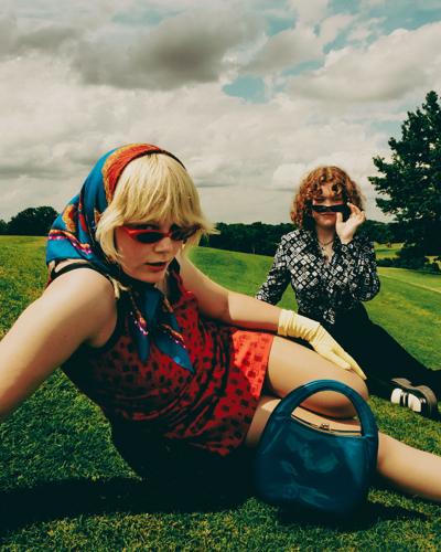 Press photo of rock duo Girl Tones, with the two members of the band sitting in the grass and looking over their sunglasses at the camera