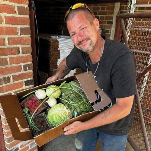 A man holds a box of fruit and vegetables, including lettuce, broccoli and raspberries.