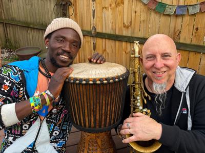 Color photo of percussionist Ibro Dioubate and sax player Jeff Coffin seated at an outdoor table with their instruments
