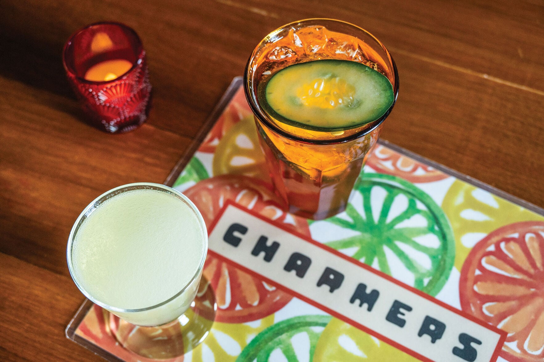 Two cocktails on a colorful napkin with lemon slice illustrations and a rectangular logo reading "Charmers"
