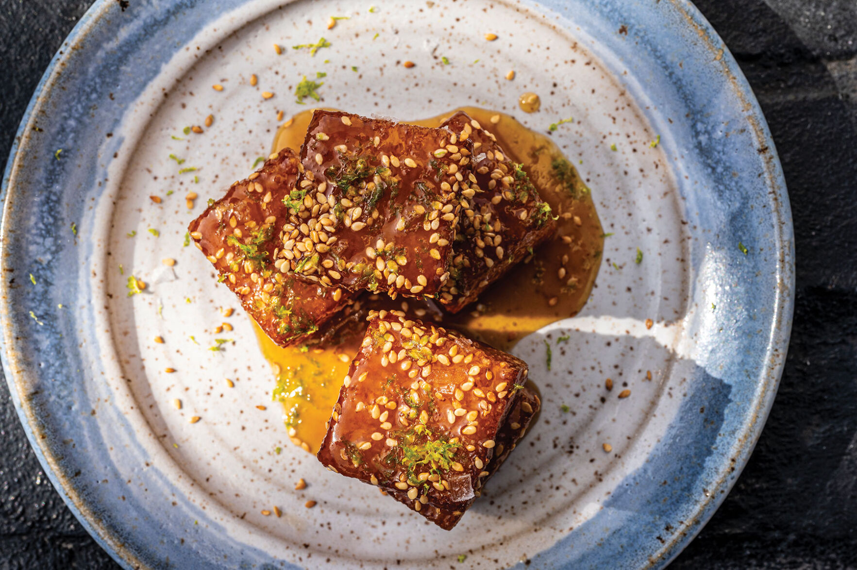 A plate of mango sticky rice, shaped into cubes and covered in sesame seeds and a sauce