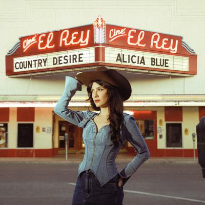 Album art for Alicia Blue’s ‘Country Desire,’ featuring a color photo of the artist in denim Western wear in the foreground, touching her hat and looking to the left. A theater called Cine El Rey is in the background with her name and the album title on the marquee.