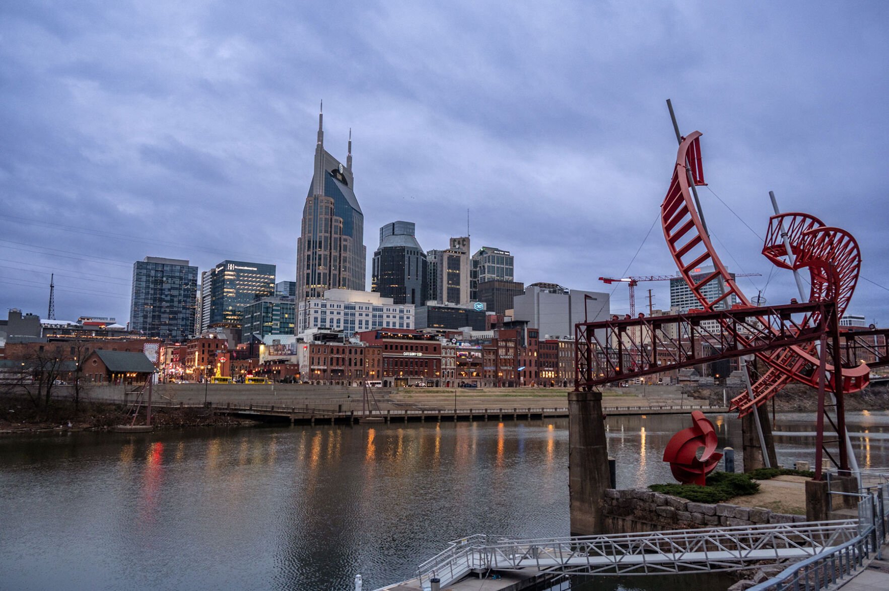 A photo of the downtown Nashville, Tenn., skyline taken in December 2025 from the East bank of the Cumberland River. The sculpture 'Ghost Ballet' is in the foreground.
