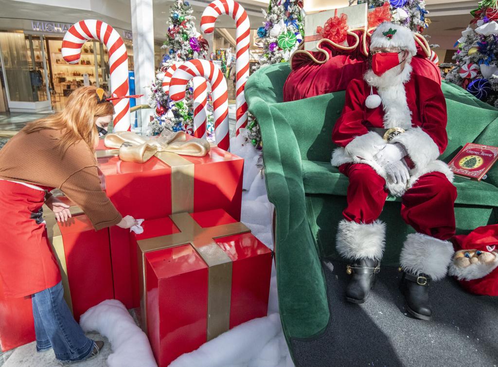 A performer dressed as Santa Claus sits behind a Plexiglas barrier