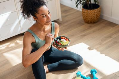 Athletic woman eating a healthy fruit bowl while sitting on floor in the kitchen at home