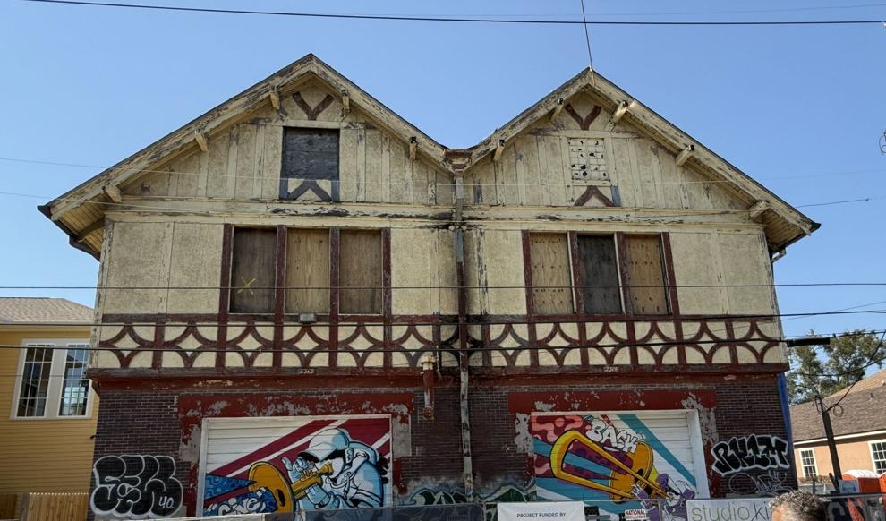 A wooden building with boarded-up windows and colorful murals over two garages at the bottom