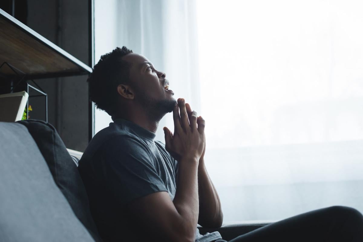 emotional african american man yelling with hands together on sofa at home (copy)