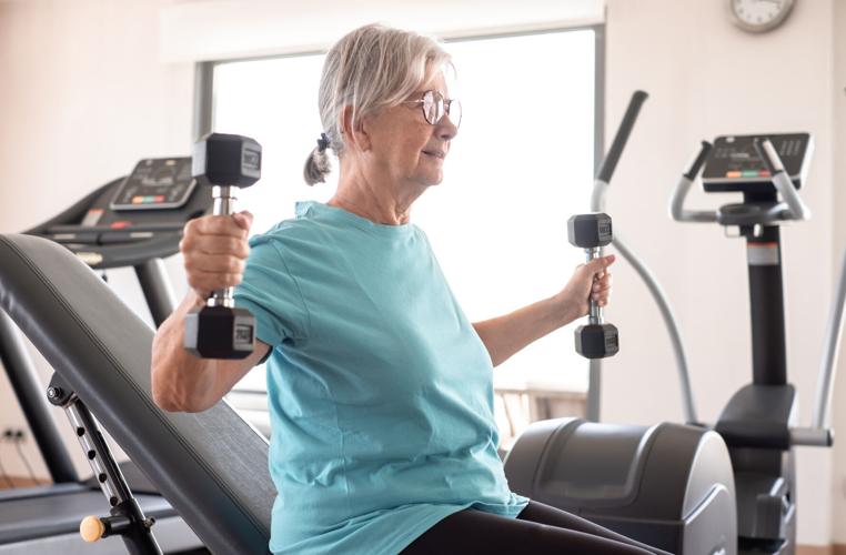 Athletic old senior woman in sportswear exercising in gym with dumbbells