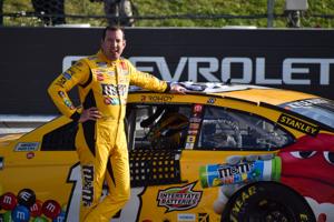 Kyle Busch poses with his No. 18 M&M's Toyota after winning the Explore the Pocono Mountains 350 Cup Series race at Pocono