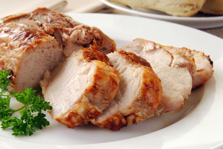 Slices of hot pork roast on a plate with herbs on the side