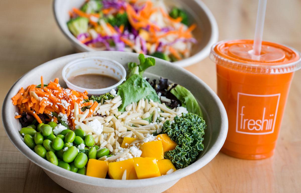 Two different Freshii salads with a carrot juice on a wooden table