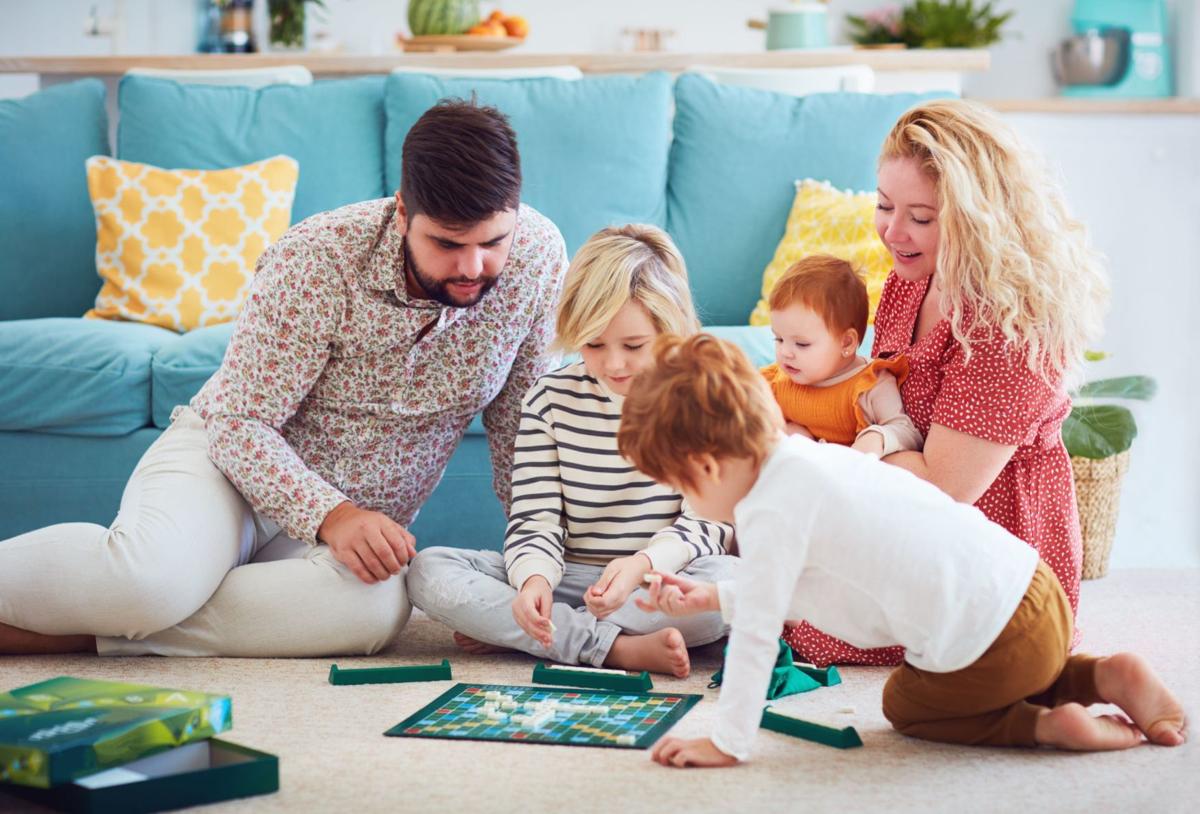  A family of five is playing a board game together on the floor in the living room.