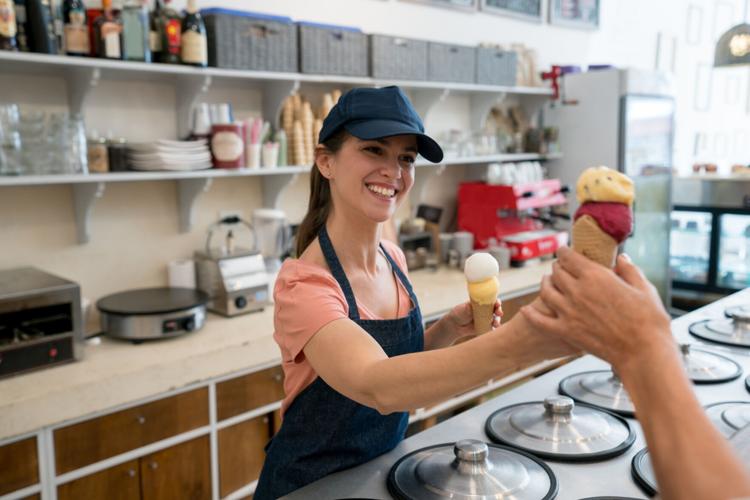 Female worker serving an ice cream to an unrecognizable customer at the ice cream parlor