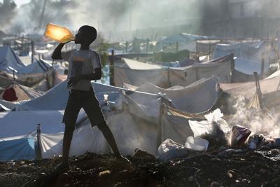 In this file photo, Rudeson Laurent, 10, takes a drink of water after brushing his teeth near a burning pile of trash inside the Daihatsu tent camp on the outskirts of Port-au-Prince, Haiti, on Jan. 25, 2010.
