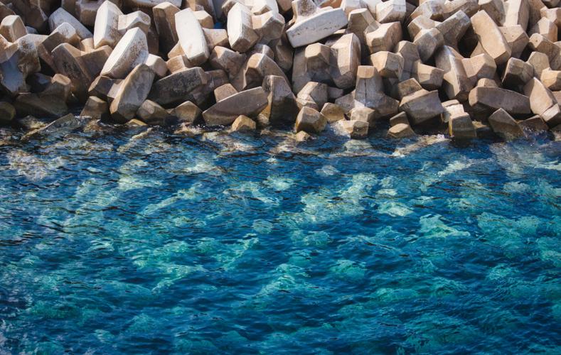 Textured background of clear blue sea and white stone tetrapods