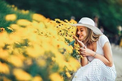 Beautiful young woman smelling yellow flower in the park.