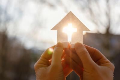 Hand with a house from paper and a cross.