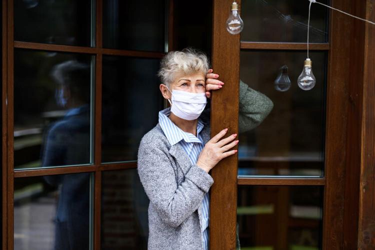 Sad senior woman standing by front door at home