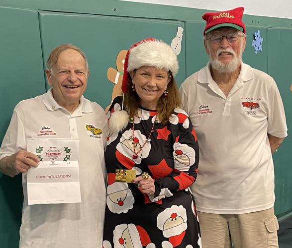 John Berson, left,  a member of the  Sunshine Corvette Club—and winner of an iHeartRadio contest—presents a $1,000 gift card to Principal Dr. Tracy Roos for a staff  appreciation lunch.   Club President  Chico Goldsmith, right, presented the school with...