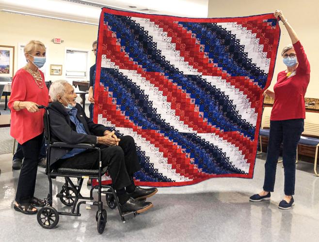 Korean War veteran Carl Zwerner and his wife, Adrianna Valdez, admire the quilt held by quilters Barbara Garvine and Linda Falls.