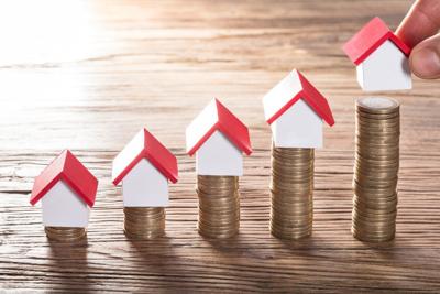 Person Placing House Models On Stacked Coins