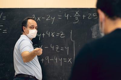 Adult teacher wearing mask explaining mathematical lessons to a student. Covid situation, pandemic, new normal.