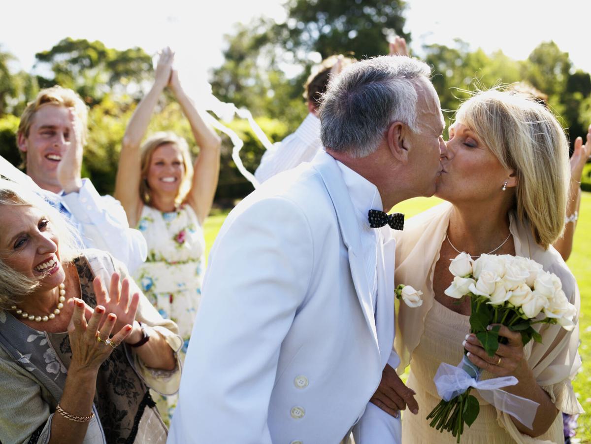 Bride and groom kissing wedding guests in background