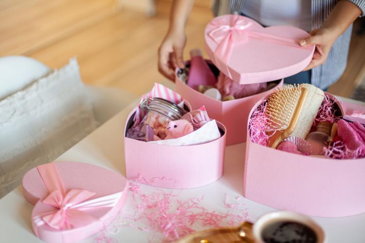 Woman hands holding pink colored heart shaped gift boxes of bath and body products for bridesmaids