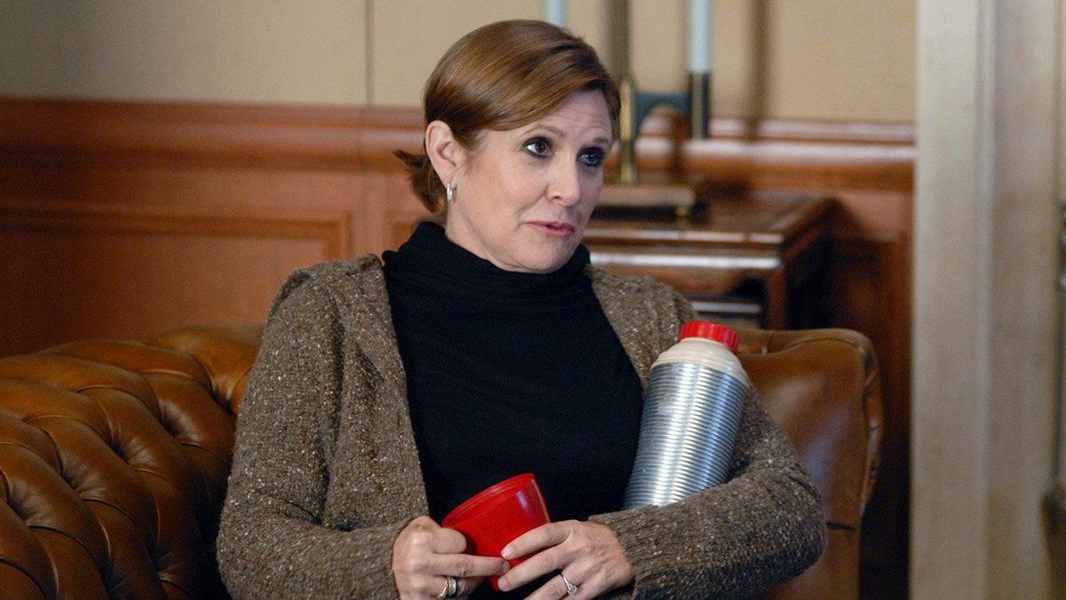 Carrie Fisher sitting on a sofa holding a thermos