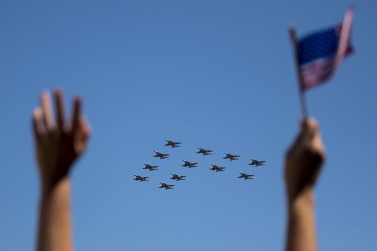 Kim Waters throws her hands in the air and waves an American flag as The Pukin Dogs of Strike Fighter Squadron 143 fly overhead as they return home from Carrier Strike Group 10 to Naval Air Station Oceana in Virginia Beach, Virginia, on April 21, 2023.