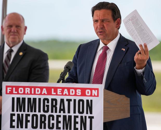 Governor Ron DeSantis holds up a sheet with crimes committed by detainees during a press conference at Alligator Alcatraz in