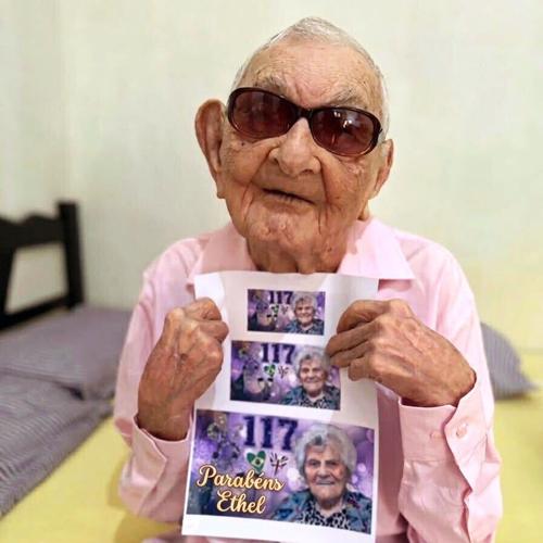 João Marinho Neto holds up a sign wishing Ethel Caterham a Happy Birthday in August 2026. Neto is 113 and has been named the world's oldest man by Guinness World Records. Caterham, 117, has been named the world's oldest person.