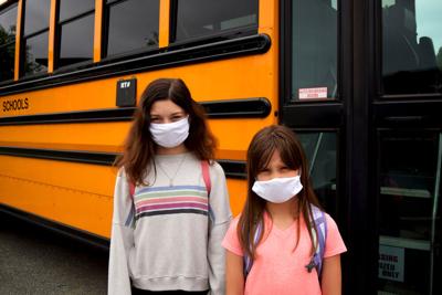 FILE - Masked kids in front of school bus