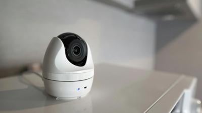 White indoor security camera placed on a tabletop in a home.