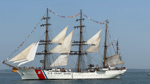 The Coast Guard Cutter Eagle sails through Boston Harbor with its sails raised.