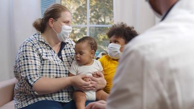 Doctor visiting multiethnic family with little children wearing protective mask