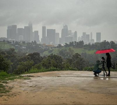 A woman holds an umbrella over a camera durin g a photo shoot on a rainy day in Elysian Park