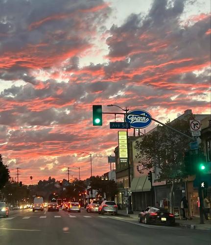 Highland Park—Street scene at dusk showing cars stopped at a green light under a vivid red and gray cloud-filled sky. A sign for “Frank’s” and a street sign for “Ave 58” are visible along the commercial stretch.