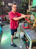 Man in red shirt smiling while pressing grapes in an outdoor workspace, part of a small backyard vineyard in Silver Lake.