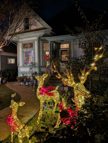 Three light-up reindeer with red bows decorate the front yard of a Lincoln Heights home at night, with holiday lights visible through the windows.