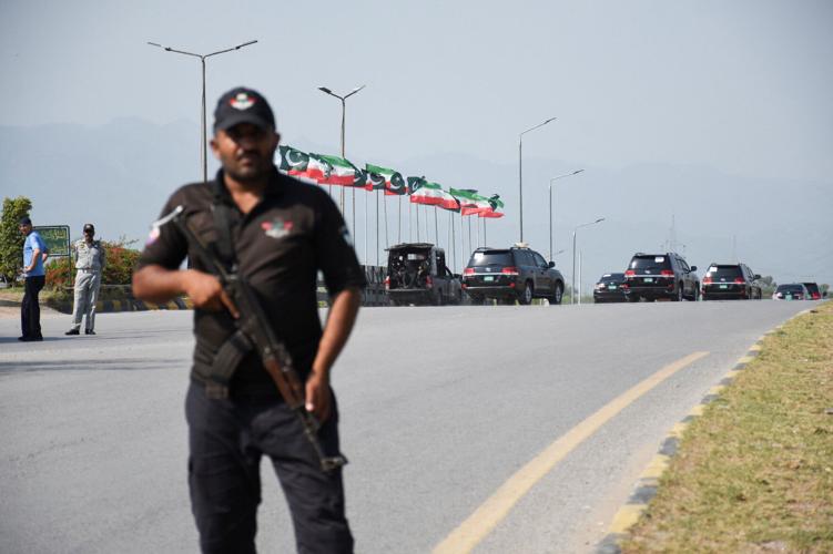 A security personnel stands guard as Pakistan's Presidential security squad vehicles carrying Iran's President Masoud Pezeshkian move past Iranian and Pakistani flags on a street in Islamabad